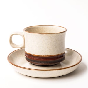 以下が含まれることがあります： ベージュの斑点のあるセラミックティーカップと、お揃いのソーサー。 カップは底に茶色のバンドと湾曲したハンドルが付いています。 ソーサーには茶色の縁があります。 ホットドリンクを提供するように設計されたセットです。
