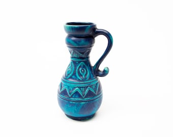 Könnte beinhalten: Eine blaue und grüne Keramikvase mit einem dekorativen Muster. Die Vase hat einen Henkel und einen runden Körper.