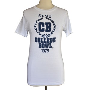May include: A white short-sleeved t-shirt featuring a dark blue graphic print on the chest. The design includes the text SFSU, CB inside a laurel wreath, COLLEGE BOWL, and the year 1978. The shirt has a crew neckline and a straight hemline.