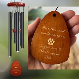 May include: A wind chime with black tubes and a wooden top and clapper. A wooden tag with the text "Hear the wind and think of me" and the name "JAX" is attached. The tag has a paw print design.
