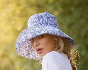 May include: A woman wearing a blue and white floral patterned sun hat. The hat has a wide brim and a soft, floppy crown.