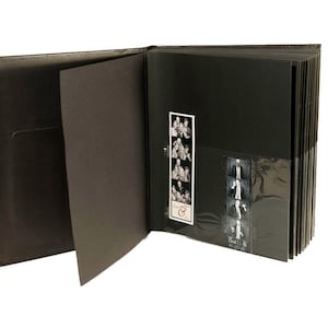 May include: Black photo album with a clear plastic sleeve on the right side, holding two strips of photo booth pictures. The album is open to reveal black pages and a pocket on the left side.