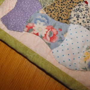May include: A patchwork quilt with a green border and a variety of floral patterns in shades of blue, pink, white, and green.
