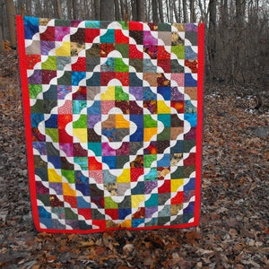 May include: A colorful quilt with a patchwork design featuring various shades of red, blue, green, yellow, and purple. The quilt is made up of squares and curved shapes, creating a unique and eye-catching pattern.