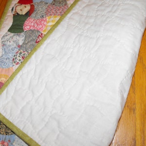 May include: A white quilt with a green border and a patchwork design on one side. The quilt is folded in half, showing the white backing.