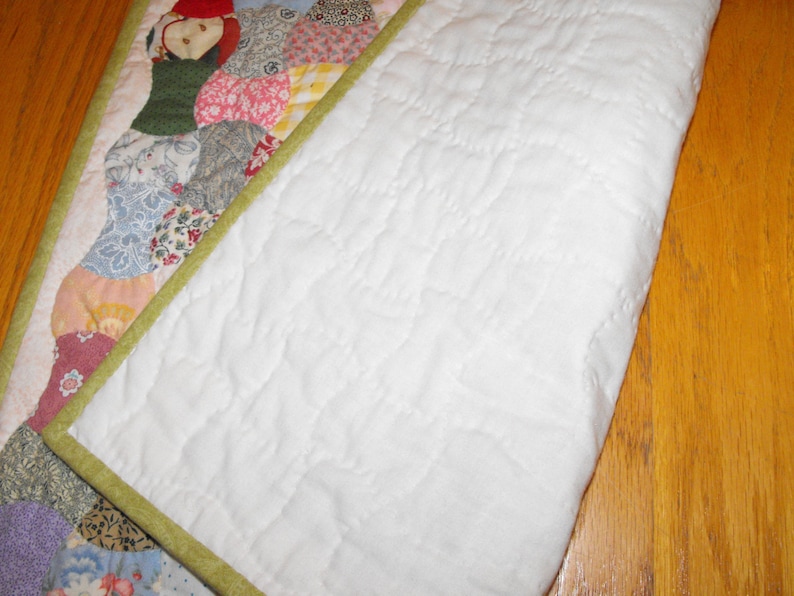 May include: A white quilt with a green border and a patchwork design on one side. The quilt is folded in half, showing the white backing.