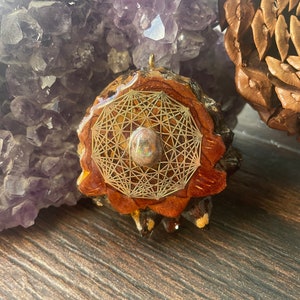 May include: A wooden pendant with a gold geometric design and an iridescent opal stone in the center. The pendant is surrounded by a brown and white wood grain.