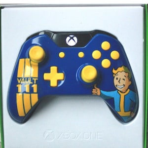 May include: Blue Xbox One controller with yellow accents and a Vault 111 design. Features a Vault Boy graphic and the Xbox logo. The controller is in a white box.