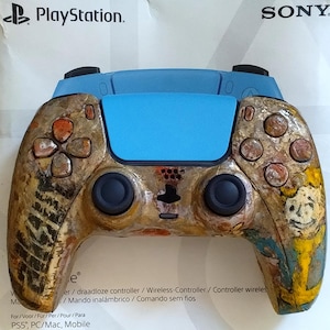 May include: A PlayStation 5 wireless controller featuring a custom textured finish with brown, tan, and yellow tones. The controller has a bright blue central touchpad, black analog sticks, and a graphic of a character on the right side.