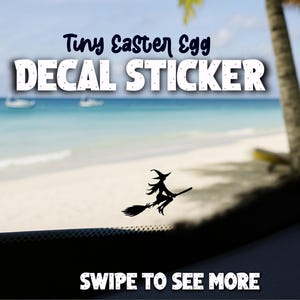 May include: A black decal sticker featuring a witch on a broomstick, with the text "Tiny Easter Egg DECAL STICKER" in white and dark blue. The background shows a beach scene with boats and palm trees.