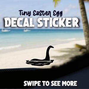 Op de afbeelding: Zwarte sticker met een silhouet van het Loch Ness Monster in water. De tekst "Tiny Easter Egg DECAL STICKER" staat boven de afbeelding. De woorden "SWIPE TO SEE MORE" staan onderaan.