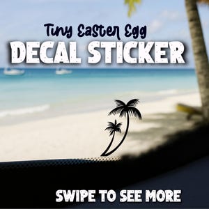 May include: A decal sticker with the text "Tiny Easter Egg DECAL STICKER" in white letters. The sticker features a black silhouette of two palm trees. The background shows a beach scene with blue water and sky.