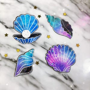 May include: Four galaxy-themed seashell stickers with blue, purple and black colours. The stickers have a glitter finish.