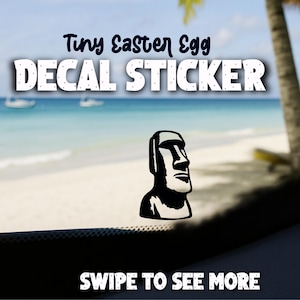 May include: A black and white decal sticker featuring a Moai statue. The text "Tiny Easter Egg DECAL STICKER" is displayed above the statue. The words "SWIPE TO SEE MORE" are at the bottom of the image.