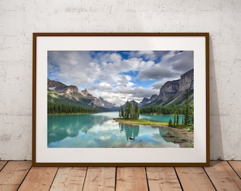 May include: A framed photograph of a mountain lake with a small island in the center. The lake is a vibrant turquoise blue and the mountains are a dark green. The sky is a light blue with white clouds.