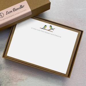 May include: A white stationery card inside a brown cardboard box. The card features two small blue and yellow birds perched on a brown branch with the printed text, A little note from Robert and Osborne. The box lid has a pink label with Lizzie Chancellor.