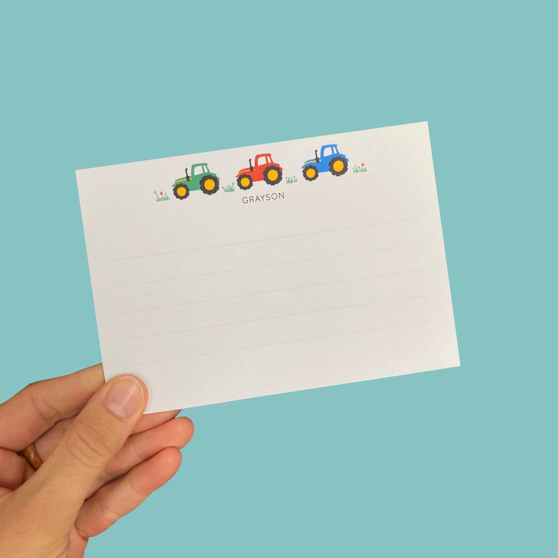May include: A white card with lined paper and a green, red, and blue tractor design at the top. The name Grayson is printed below the tractors.