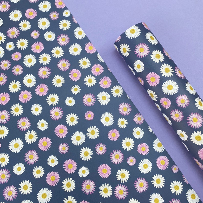 Pode incluir: Uma folha de papel de embrulho azul com um padr&atilde;o repetitivo de margaridas brancas e rosa. O papel est&aacute; dobrado ao meio e as bordas s&atilde;o vis&iacute;veis.