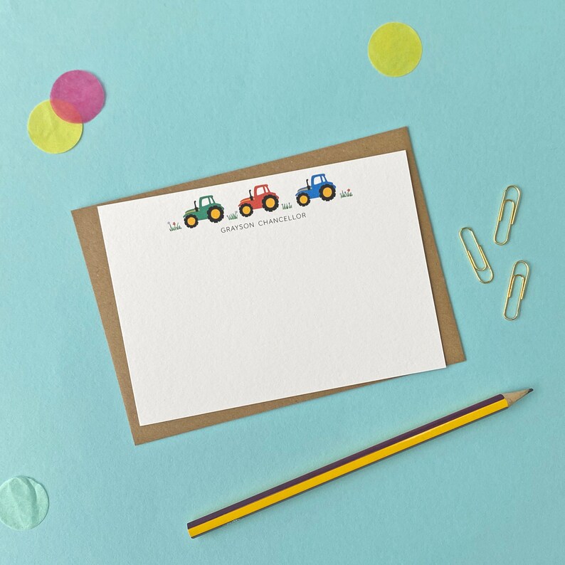 May include: A white card with a brown border features a line of three toy tractors in green, red, and blue. The text "GRAYSON CHANCELLOR" is printed below the tractors.