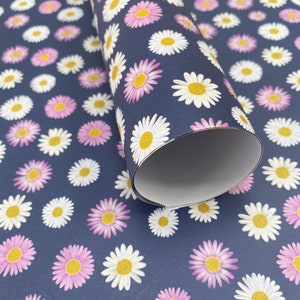 Pode incluir: Um rolo de papel de embrulho azul com um padr&atilde;o de margaridas brancas e rosa. O papel est&aacute; enrolado e a extremidade &eacute; vis&iacute;vel.