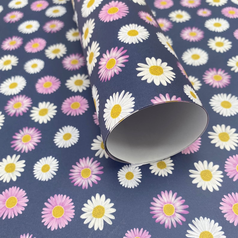 Pode incluir: Um rolo de papel de embrulho azul com um padr&atilde;o de margaridas brancas e rosa. O papel est&aacute; enrolado e a extremidade &eacute; vis&iacute;vel.