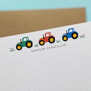 May include: A white card with three toy tractors in a line. The tractors are green, red, and blue. The card has the name "GRAYSON CHANCELLOR" printed on it.