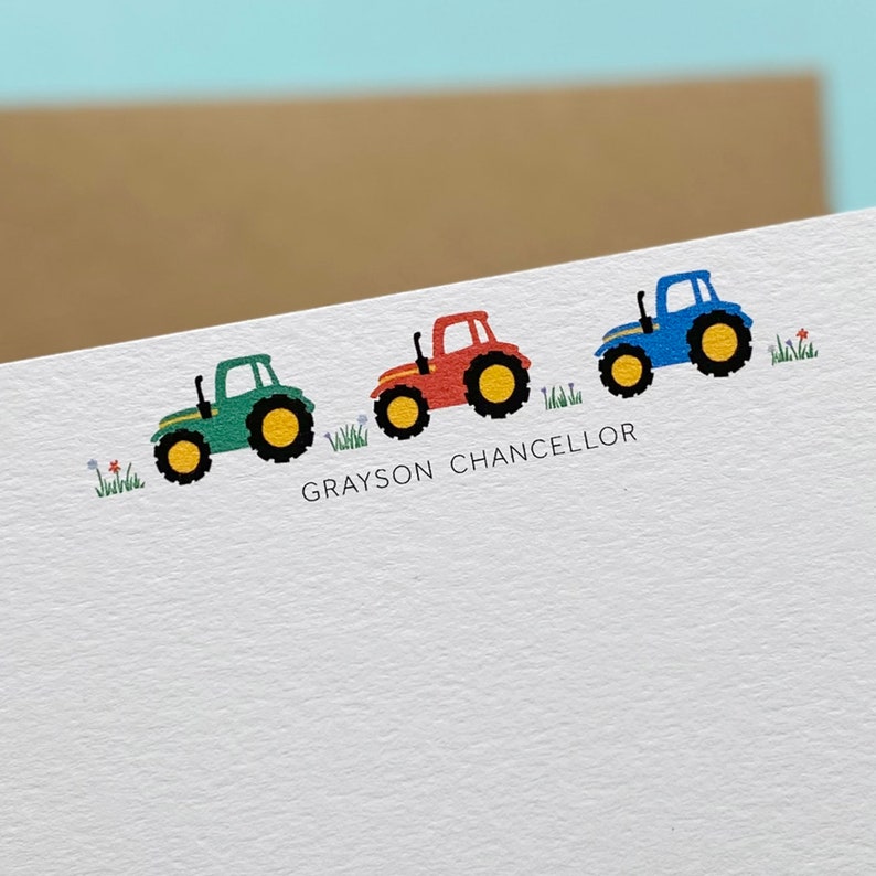 May include: A white card with three toy tractors in a line. The tractors are green, red, and blue. The card has the name "GRAYSON CHANCELLOR" printed on it.