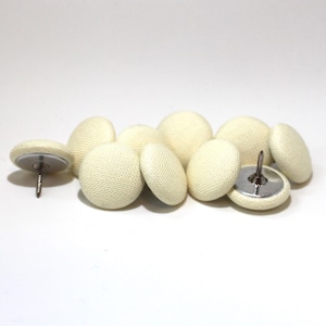 May include: A group of eight off-white fabric covered buttons with a silver tack on the back. The buttons are arranged in a semi-circle.
