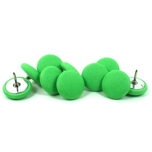 May include: A collection of bright green fabric-covered push pins. The pins have a circular, button-like appearance with a silver metal base and a sharp pin extending from the center. The fabric has a textured weave.