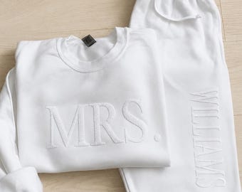 Puede incluir: Un conjunto de descanso blanco a juego que consta de una sudadera de cuello redondo y pantalones de chándal. La sudadera presenta el texto bordado MRS. en blanco, mientras que los pantalones tienen el texto WILLIAMS bordado verticalmente.