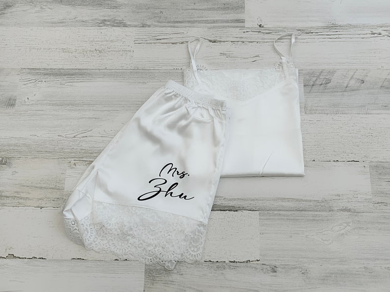 May include: White satin pajama shorts with lace trim and the text "Mrs. Zhu" in black script. The shorts are paired with a white satin tank top with lace trim.