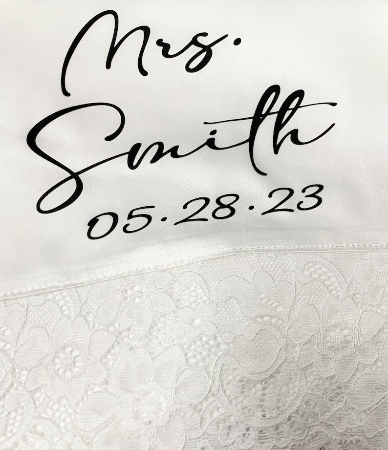 May include: White satin robe with black lace trim and the text "Mrs. Smith 05.28.23" embroidered on the front.