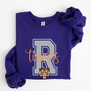 May include: Purple sweatshirt with a gray letter R and the word "tigers" in orange script. A tiger head is inside the letter R.