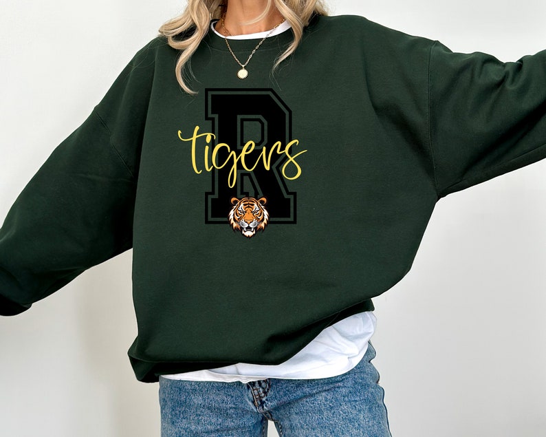May include: A dark green sweatshirt with a black and white letter "R" and the word "tigers" in yellow lettering. A tiger face is inside the letter "R".