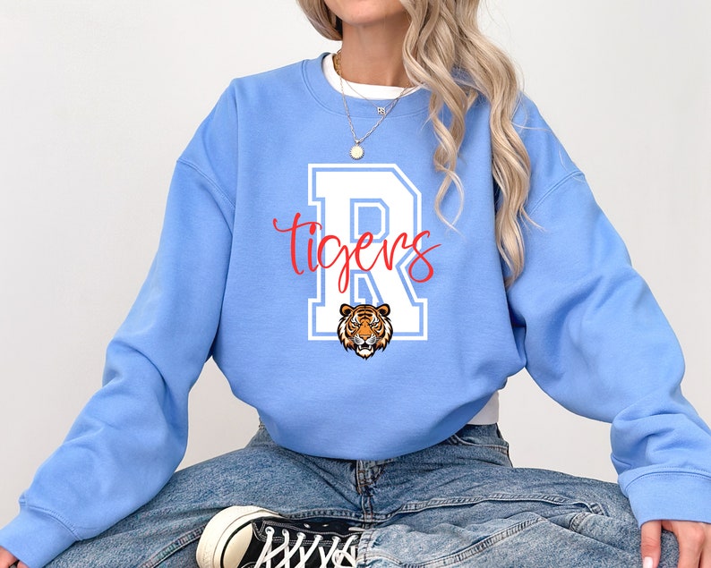 May include: A light blue sweatshirt with a white letter "R" and the word "tigers" in red. The letter "R" has a white outline and a tiger head inside.