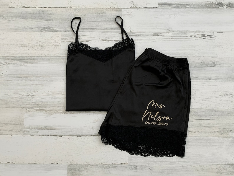 May include: Black satin pajama set with lace trim. The shorts have the text "Mrs. Nelson 06.09.2023" embroidered in gold.