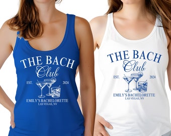 May include: Two tank tops with the text "THE BACH Club" and a graphic of cocktails. The text "EST. 2024" and "EMILY'S BACHELORETTE LAS VEGAS, NV" are also included on the tank tops. One tank top is blue and the other is white.