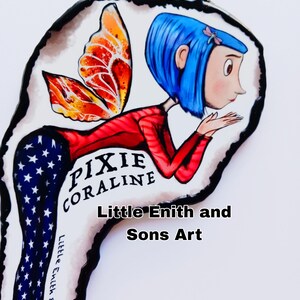 May include: A whimsical illustration of a character named Pixie Coraline with blue hair, a red top, and star-spangled pants. The character has orange and red wings. The text "Pixie Coraline" and "Little Enith and Sons Art" are also visible.