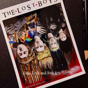 May include: A rectangular print featuring the text "THE LOST BOYS" at the top. The artwork depicts four individuals with varying hair colors and styles. The bottom of the print includes the text "Little Enith and Sons Art".