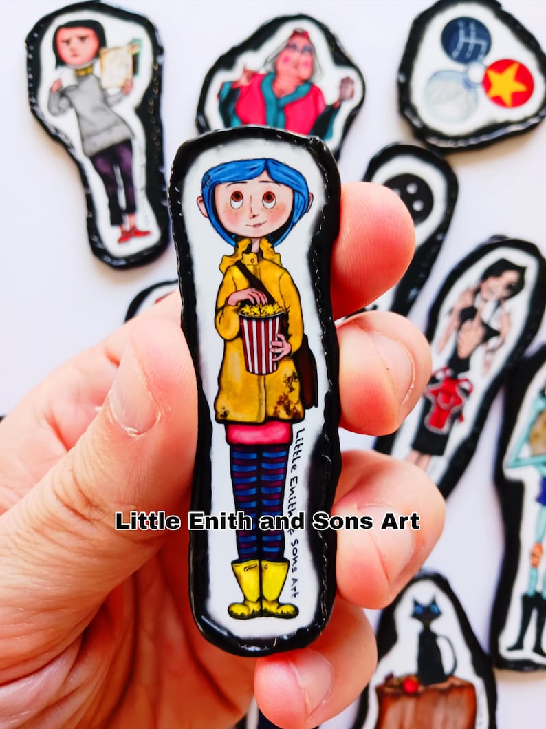 May include: A collection of handmade art pieces featuring characters from the animated film "Coraline." The central piece depicts a girl in a yellow raincoat holding popcorn. Other pieces show various characters. The text "Little Enith and Sons Art" is visible.