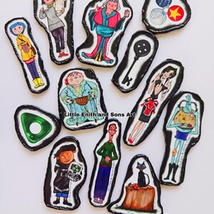 May include: A collection of illustrated character magnets with black borders. The magnets feature characters from a movie, including a girl in a yellow raincoat, a woman in a red dress, and a black cat. The text "Little Enith and Sons Art" is visible.
