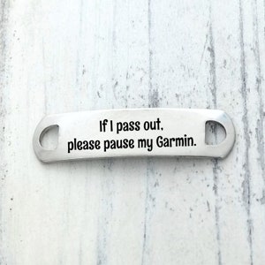 May include: A silver-toned metal shoe tag with a curved rectangular shape and two circular holes on the ends. The surface is engraved with the black text: If I pass out, please pause my Garmin. The tag has a smooth, polished finish.