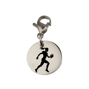 May include: A circular silver-toned metal charm featuring a black silhouette of a person running while holding an American football. The charm is attached to a silver-toned lobster claw clasp, designed for easy attachment to bracelets or necklaces.