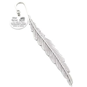 May include: Silver feather bookmark with a round charm that reads "Altar Server Our Lady of Peace Korean Catholic Center CELESTINE CHUNG 2019 to 2024".