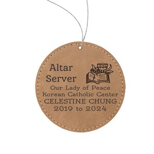 May include: A brown leather ornament with the text "Altar Server Our Lady of Peace Korean Catholic Center CELESTINE CHUNG 2019 to 2024".