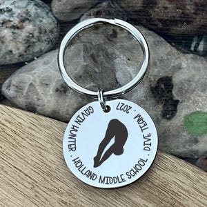 May include: A silver keychain with a round pendant featuring a diver silhouette. The pendant has the text "Gavin Hunter," "Dive Team," "Holland Middle School," and "2027" around the edge. The diver is in mid-dive.