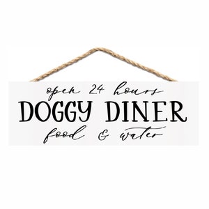 May include: White wooden sign with black text that reads "open 24 hours Doggy Diner food & water". The sign has a rope hanger.