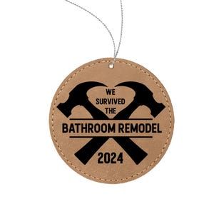 May include: Brown leather ornament with a black silhouette of two crossed hammers and the text "We survived the bathroom remodel 2024".