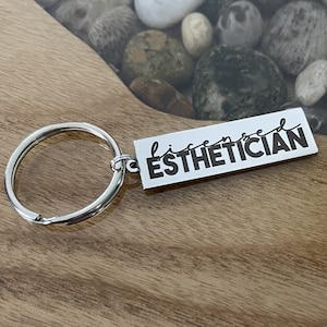 May include: Silver keychain with a rectangular tag that says "licensed esthetician" in black lettering.