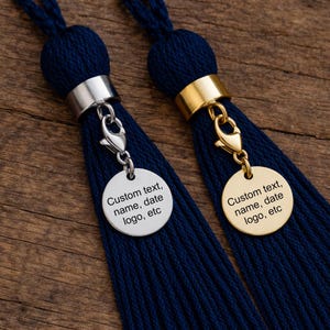 May include: Two navy blue tassels with metal accents. One has a silver-colored band and clasp, the other gold. Each has a round tag with the text "Custom text, name, date, logo, etc."